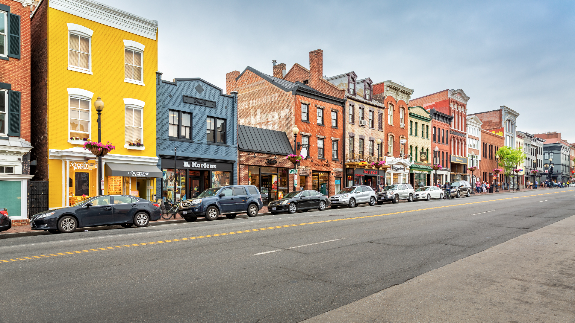 Row of colorful main-street storefronts with parked cars along the curb